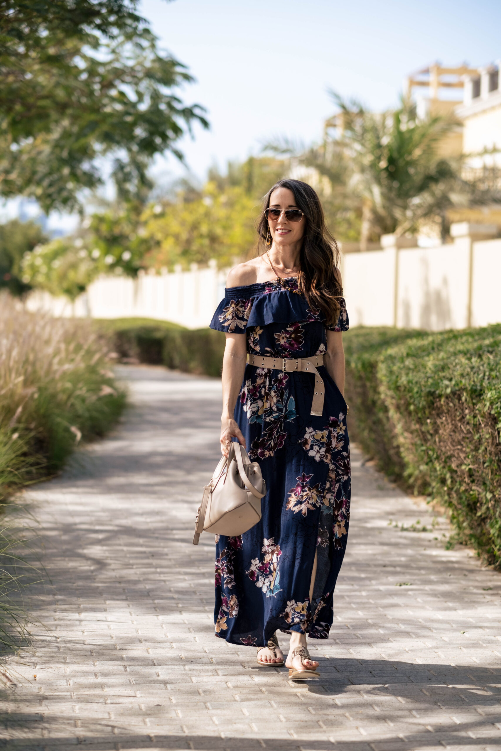 Walking to camera with floral off the shoulder dress, neutral belt, bag and rose gold sunglasses