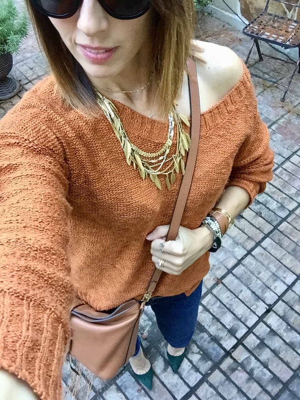 A woman wearing an orange sweater and holding onto a brown purse.