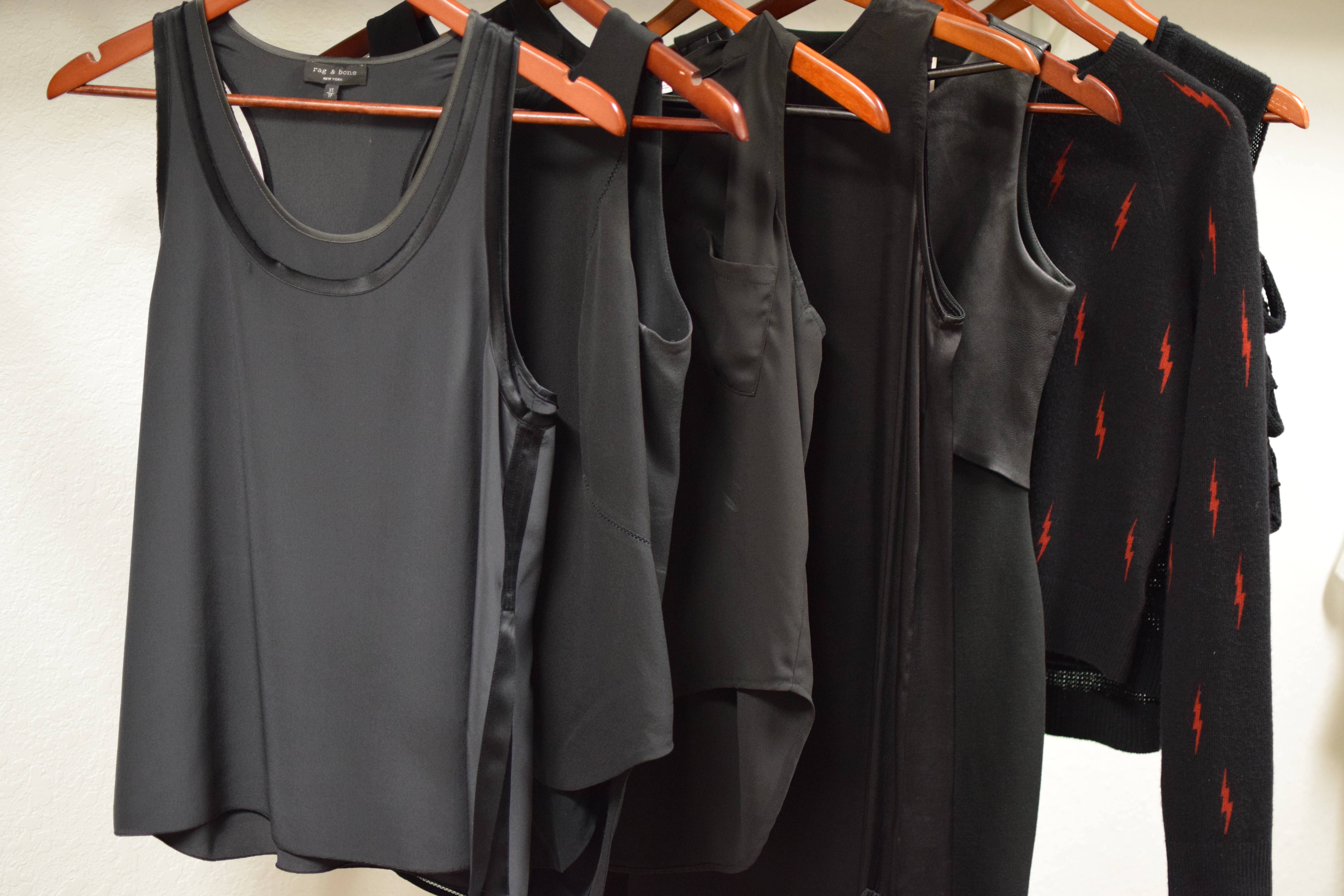 A row of black shirts hanging on wooden hangers.