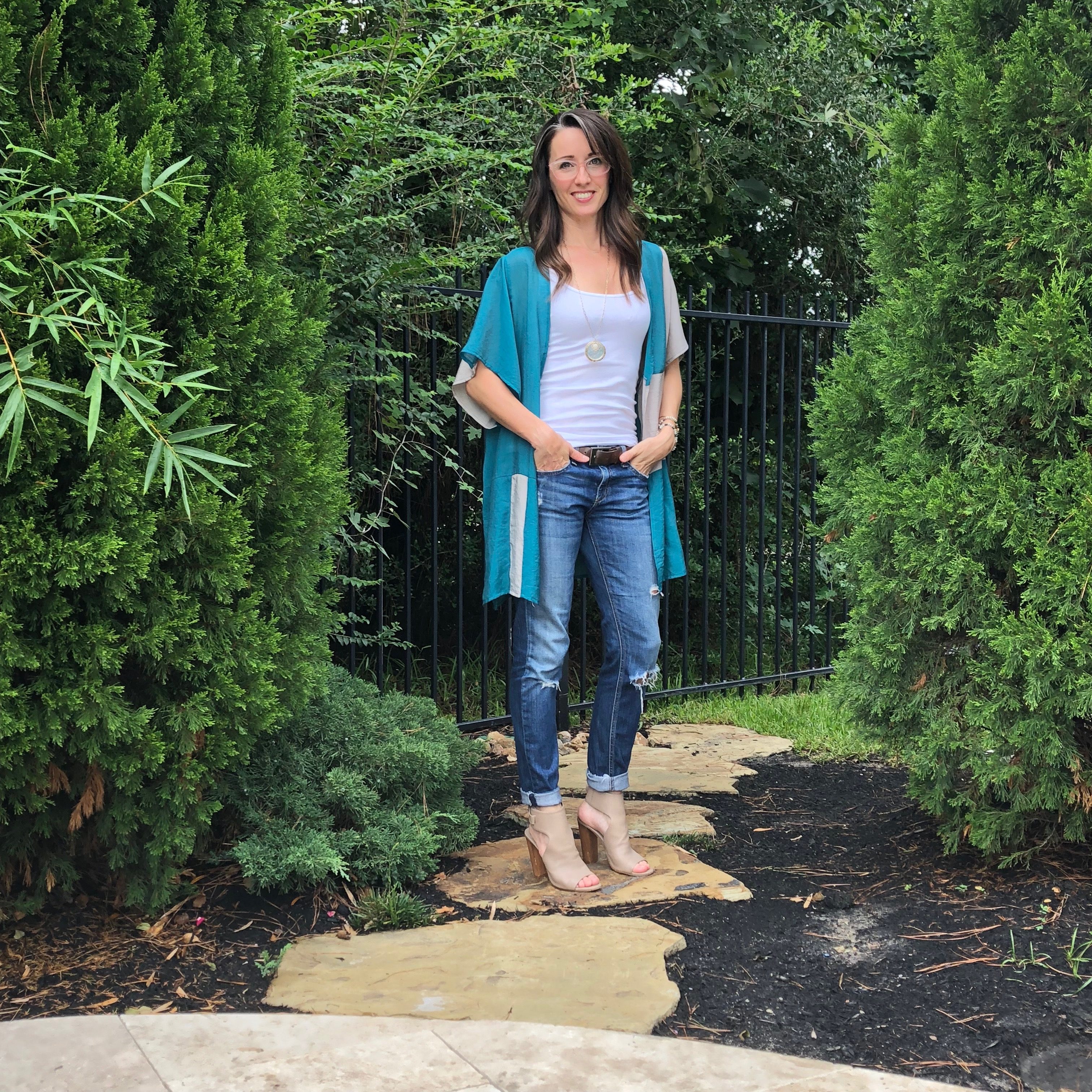 A woman standing on the side of a path in front of bushes.