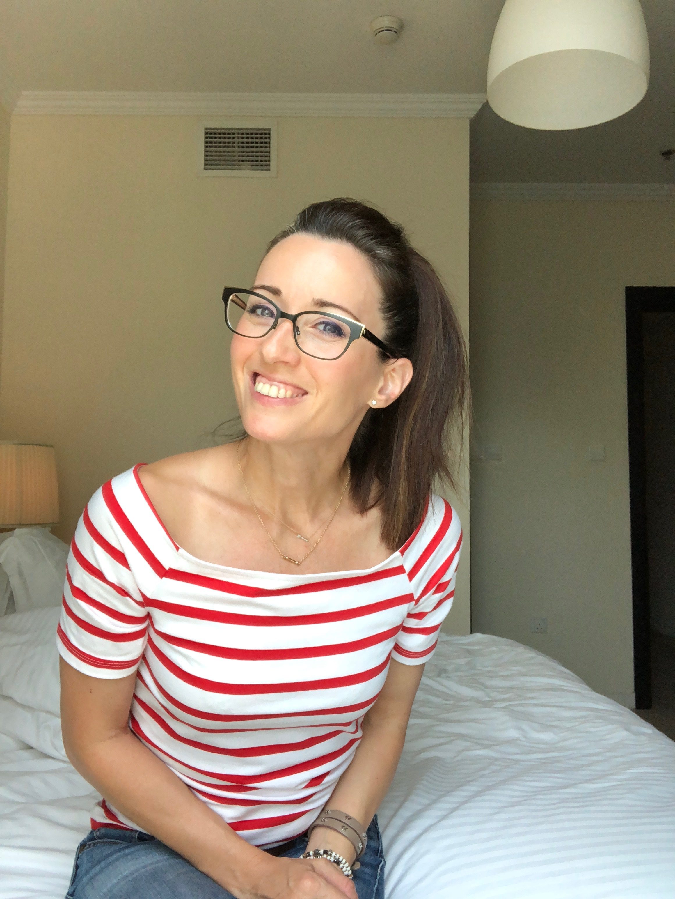 A woman sitting on top of a bed wearing glasses.