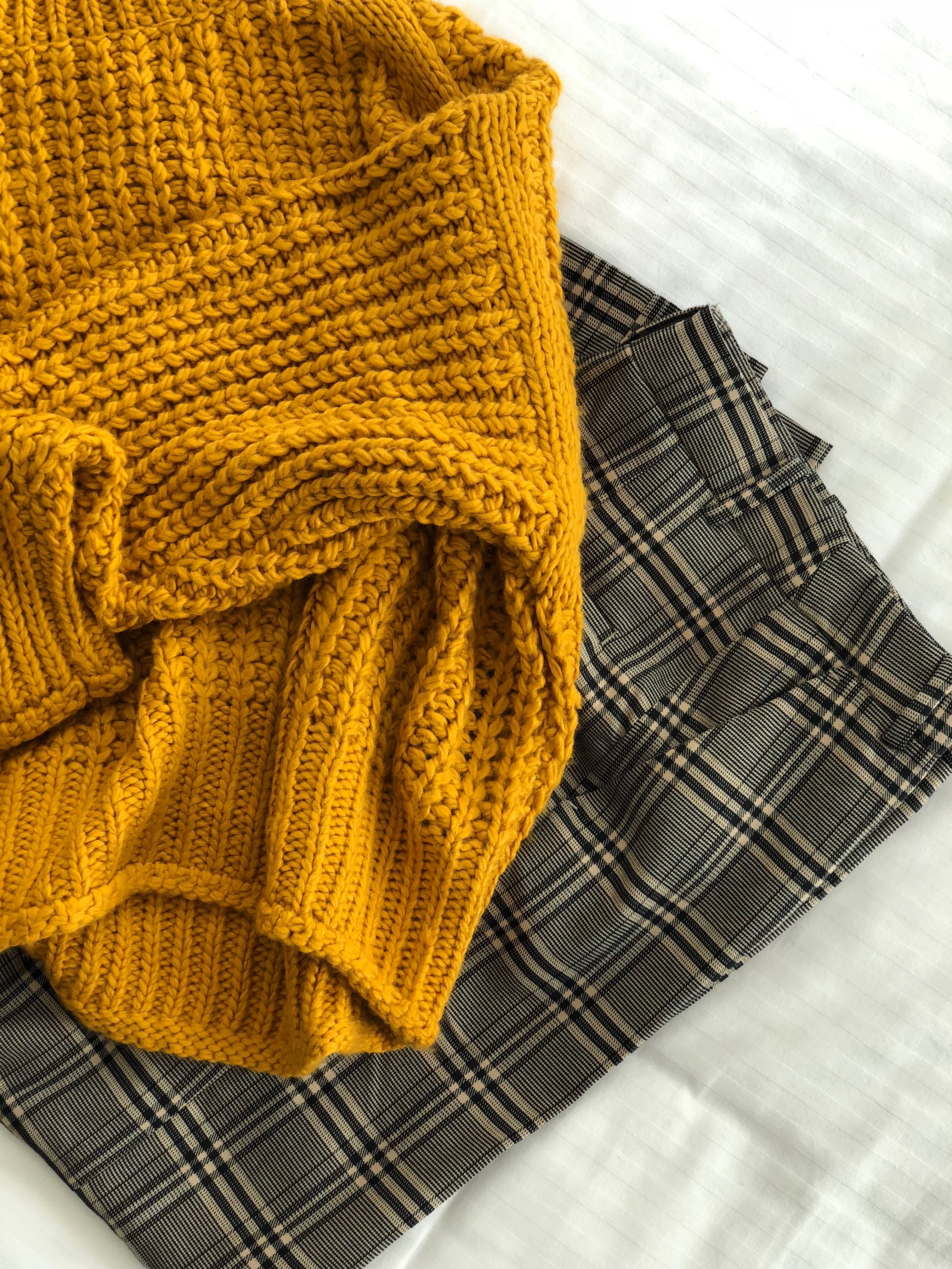 A yellow sweater on top of a plaid blanket.