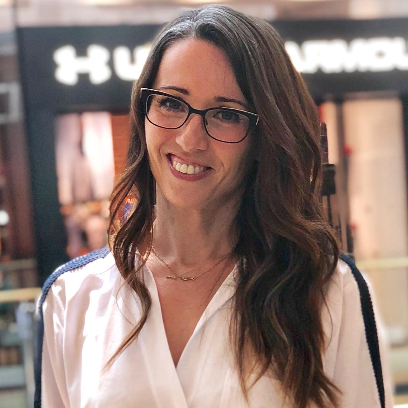 A woman with glasses standing in front of a store.