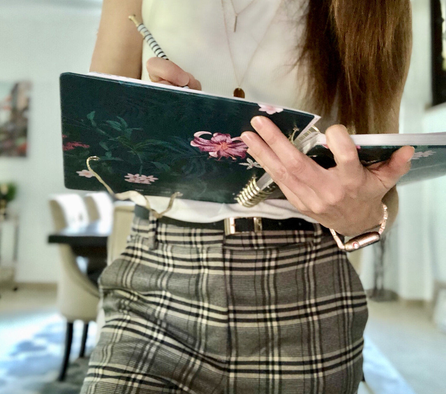 A woman is holding her laptop and wearing plaid pants.