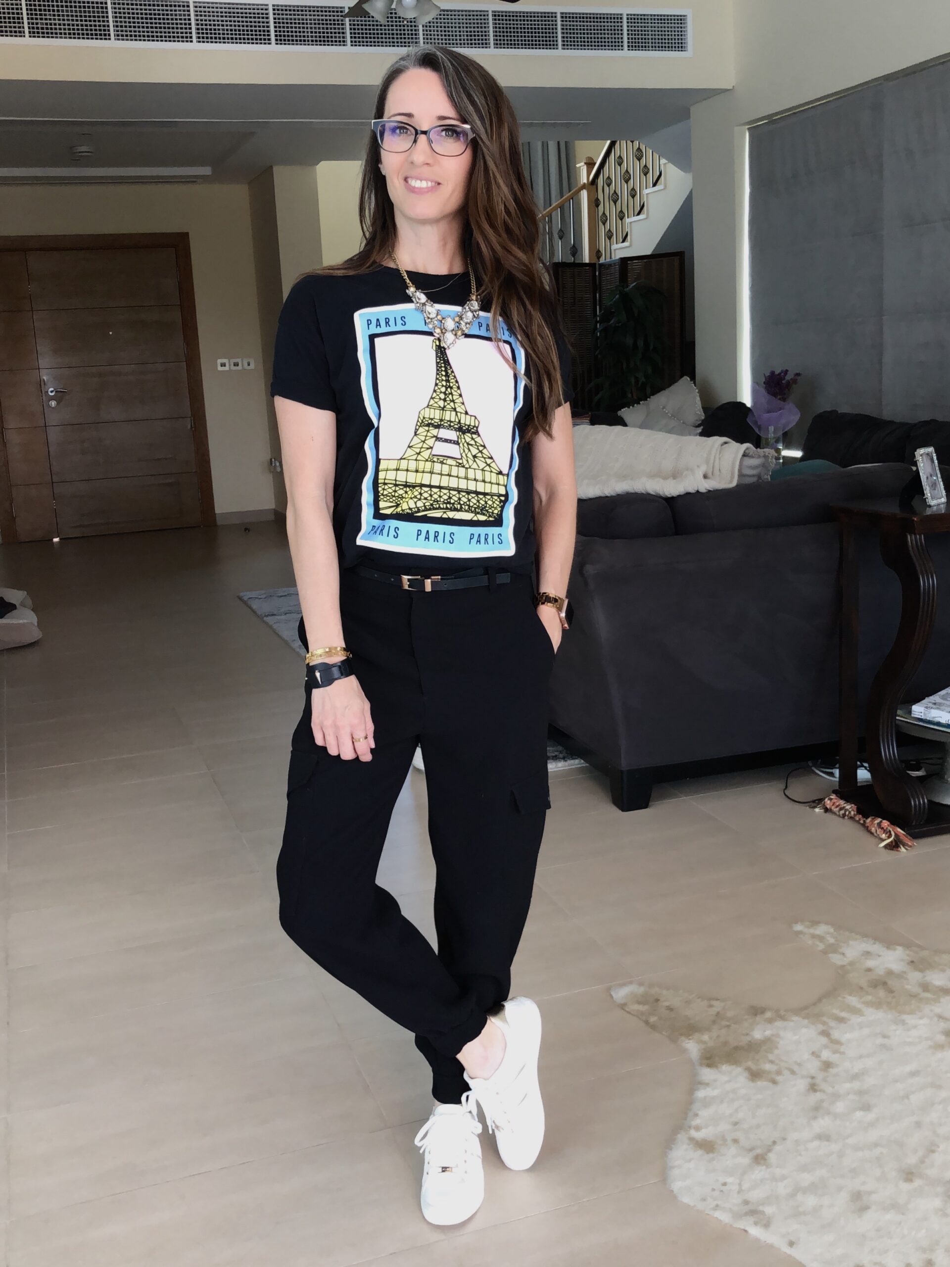 A woman standing in front of a couch wearing white sneakers.