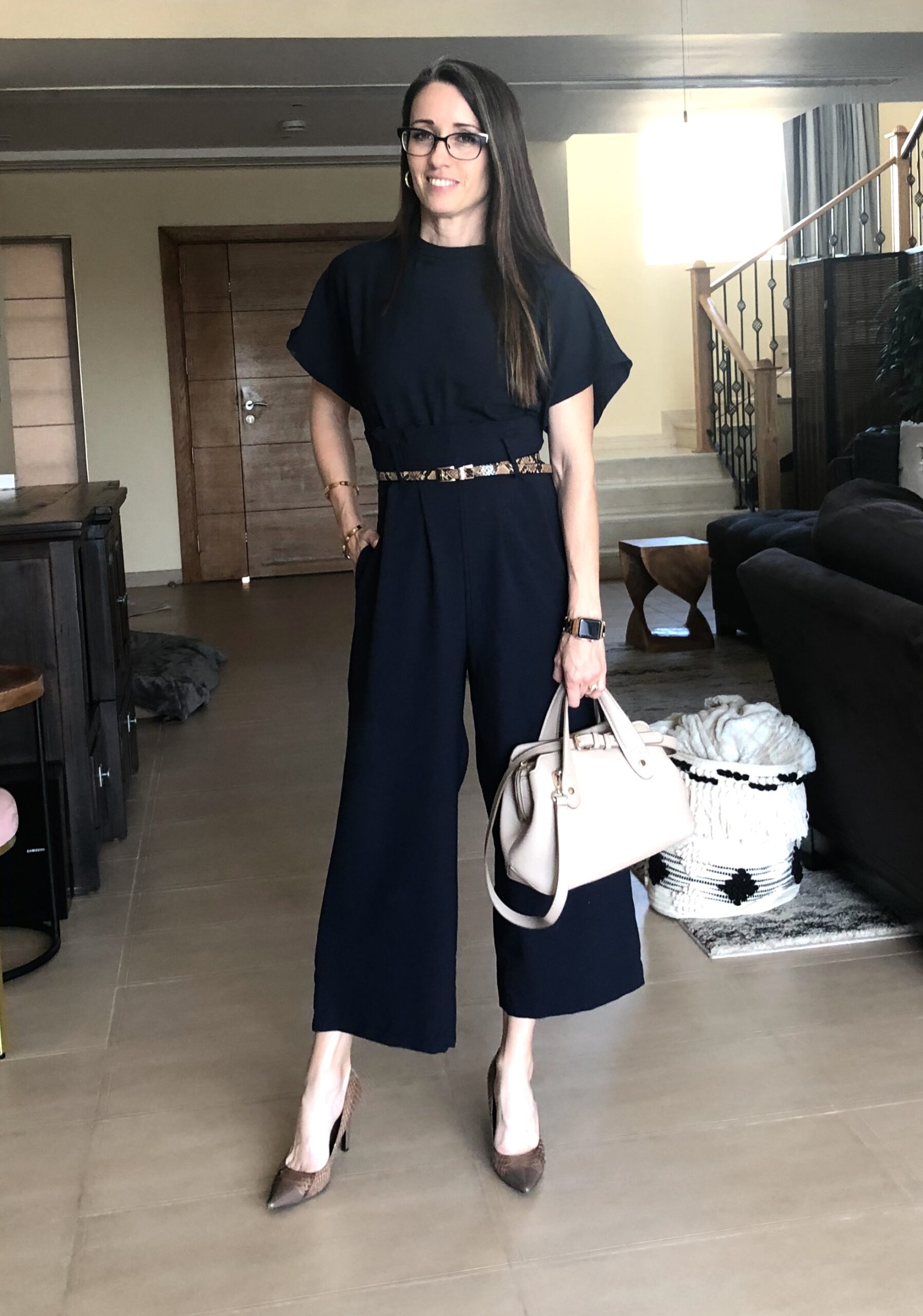 A woman standing in front of a living room holding onto a white purse.