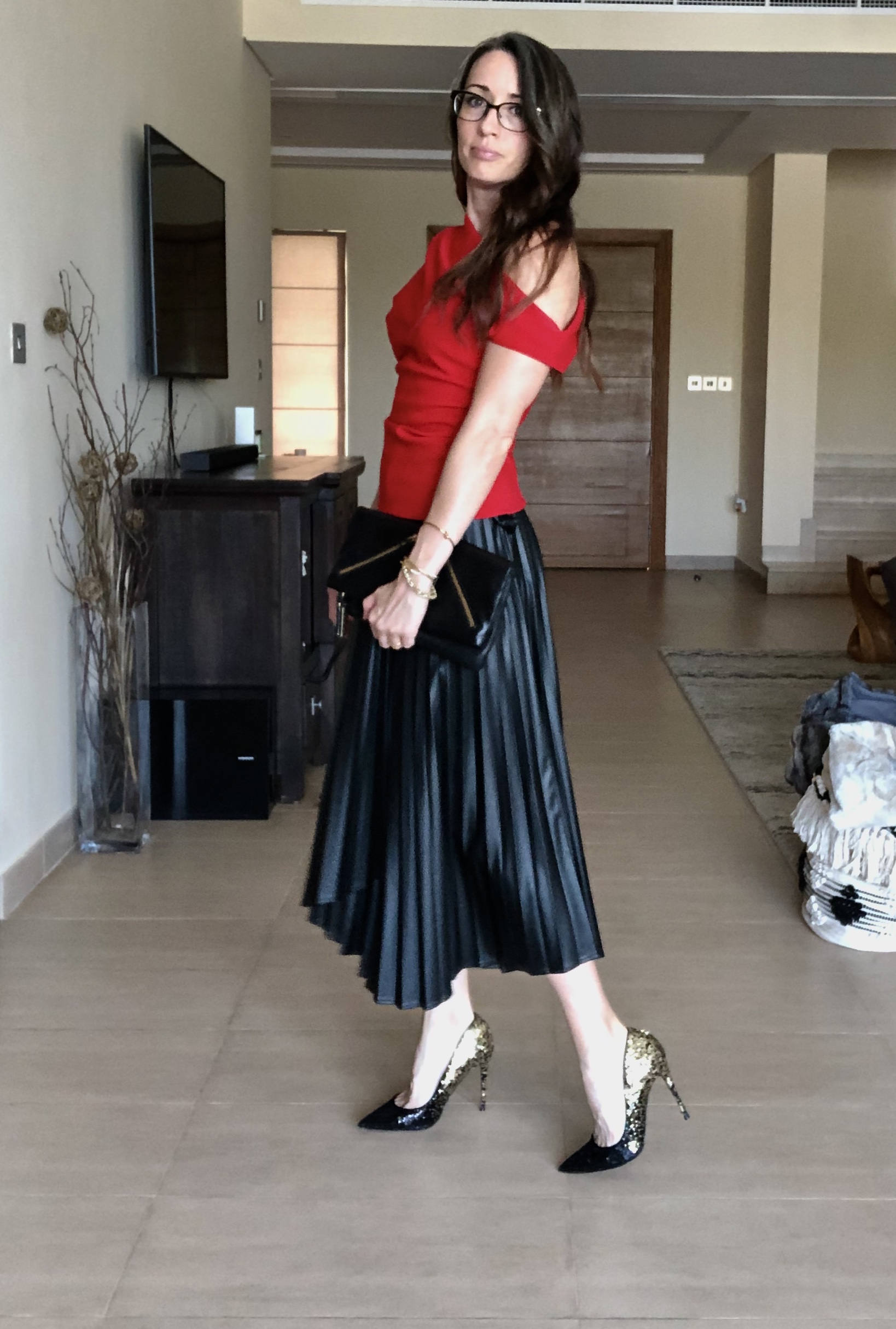 A woman in red shirt and black skirt holding purse.