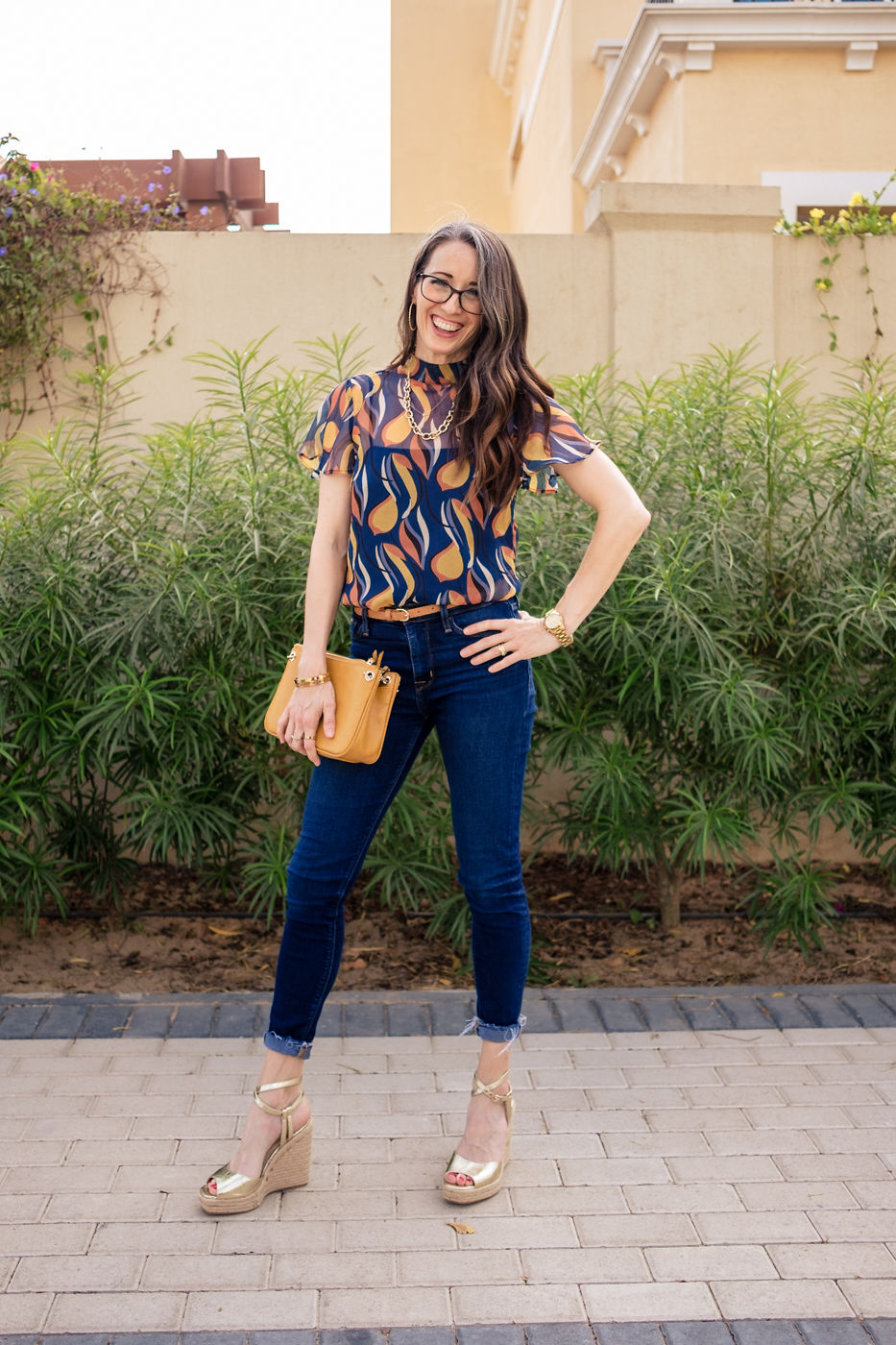 A woman standing on the sidewalk wearing jeans and heels.